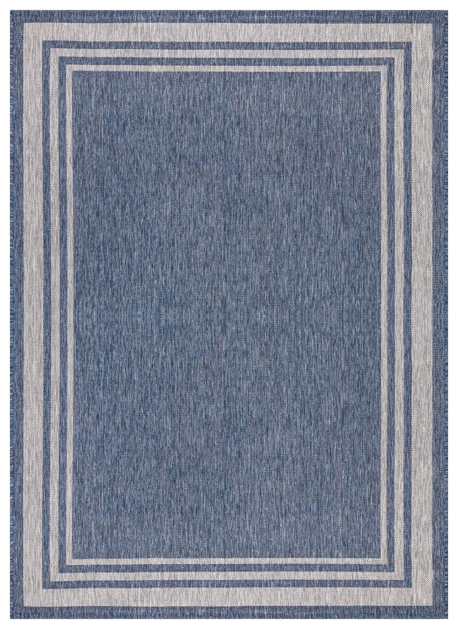 Navy and ivory bordered outdoor rug on covered teak patio
