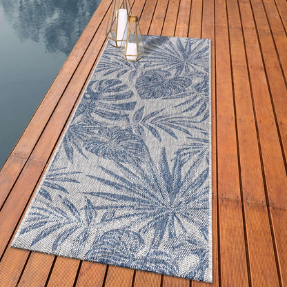 Lush monstera and palm outdoor rug styled with rattan dining furniture