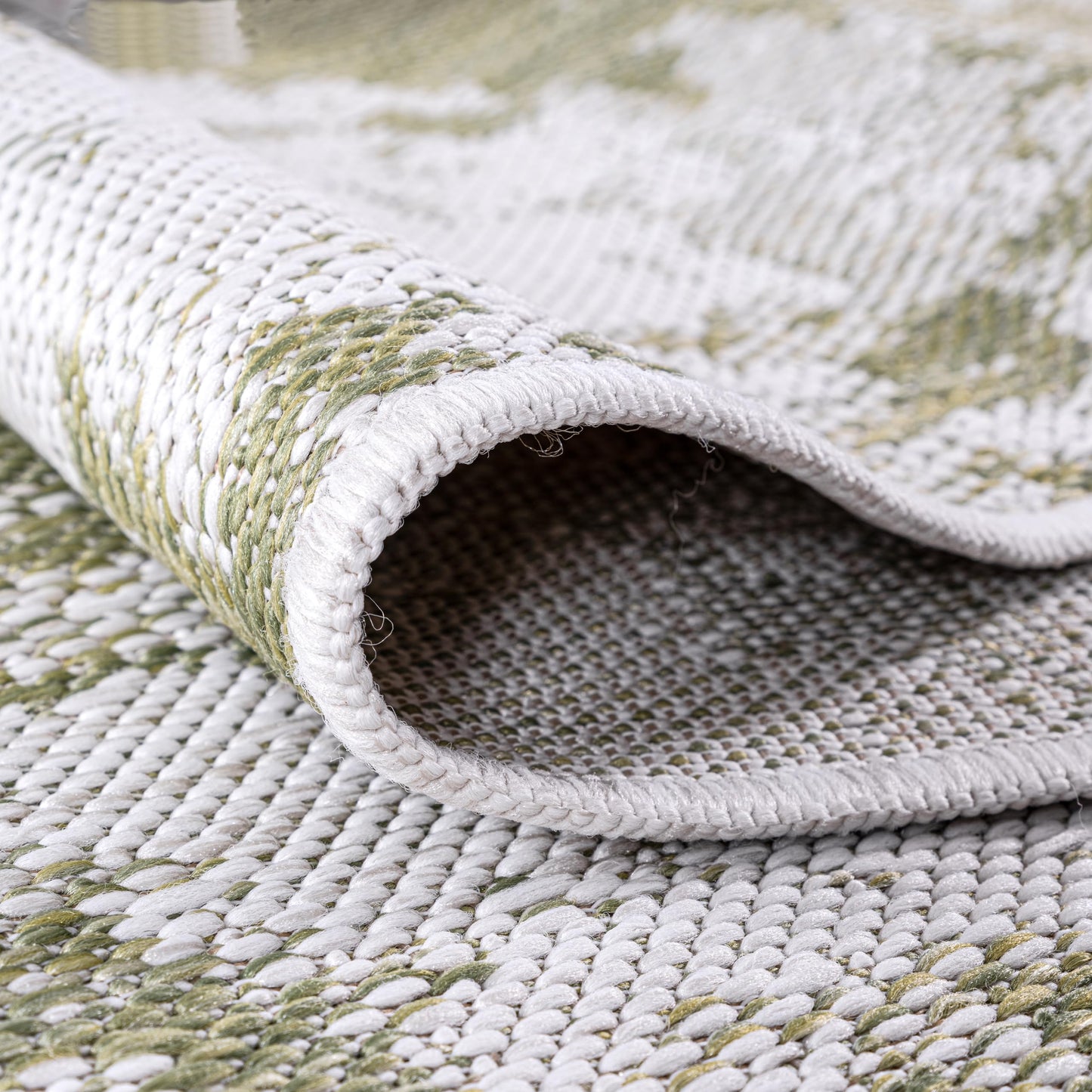 Green painterly rug in three-season sunroom with rattan furniture